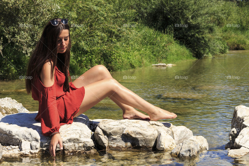 Beautiful woman sitting on rock in lake