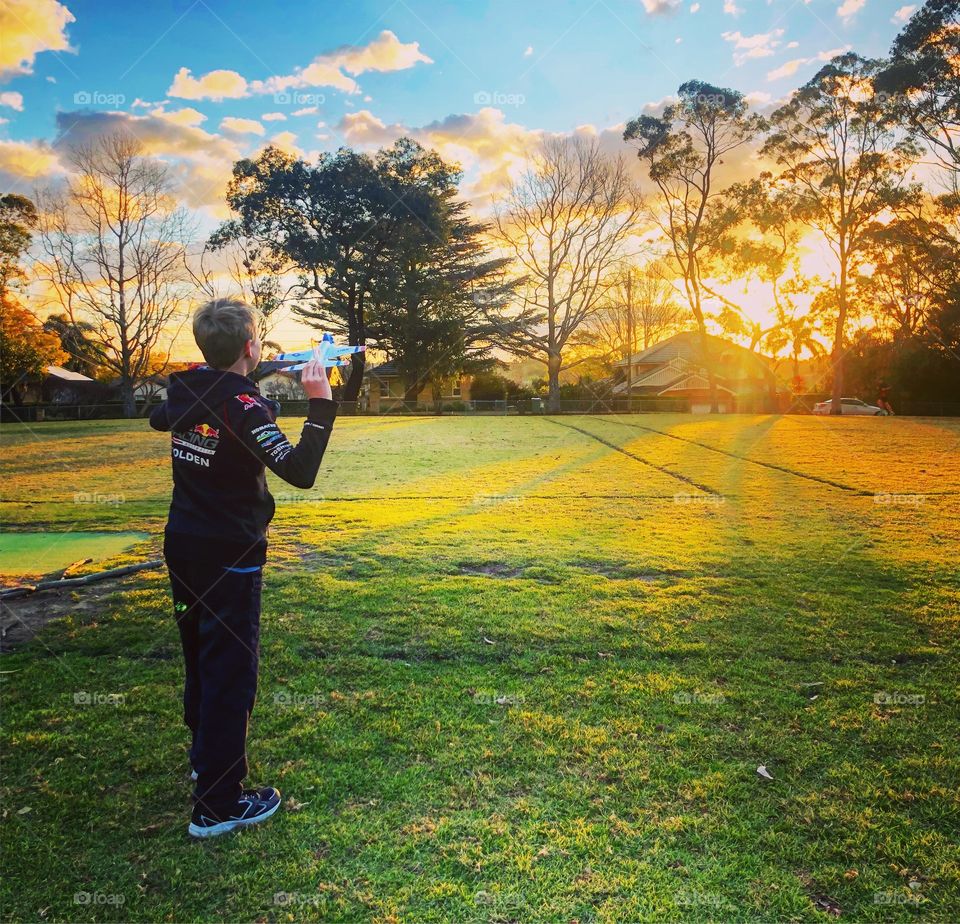 At the park at sunset, flying a toy plane 