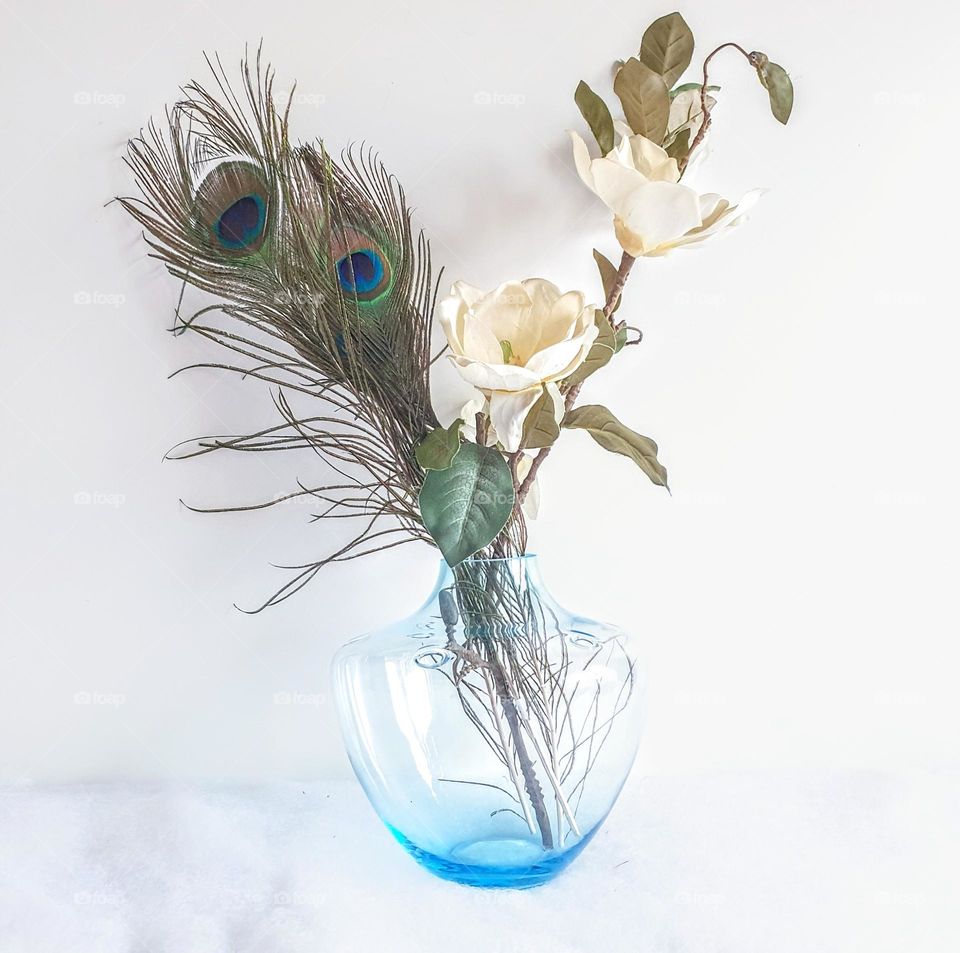 clean light and bright high key still life with blue translucent glass vase filled with flowers and peacock feathers