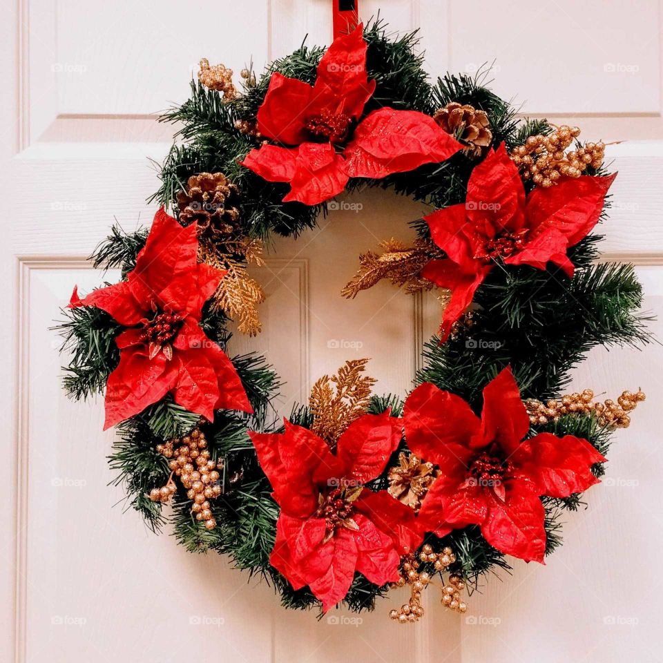 A holiday door wreath with pine cones and poinsettia flowers