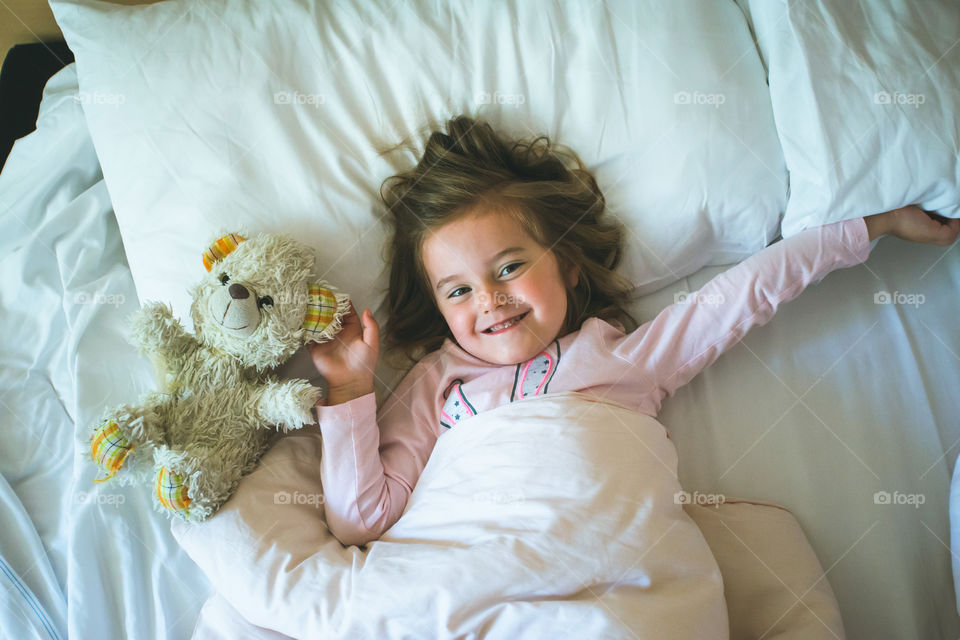 Little girl lying in a bed with teddy bear at the morning