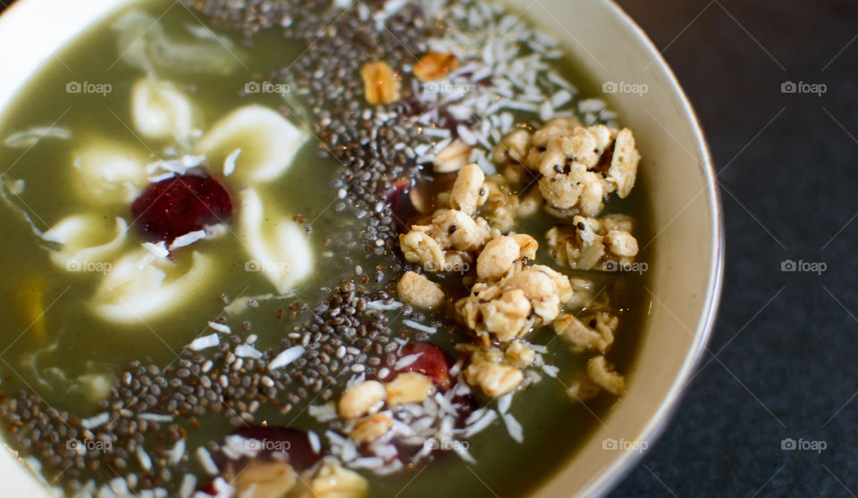 Beautiful green smoothie bowl with sweet Coconut, dark chia, oatmeal clusters, red cherry and yogurt white flower design artisanal healthy food background closeup photography 