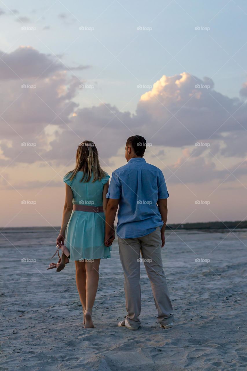 young couple in love on the beach at sunset with their backs to the camera, summer time of the year