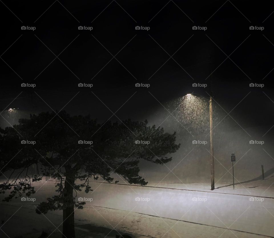 Snow falling in cones of light under streetlights on a quiet winter street 