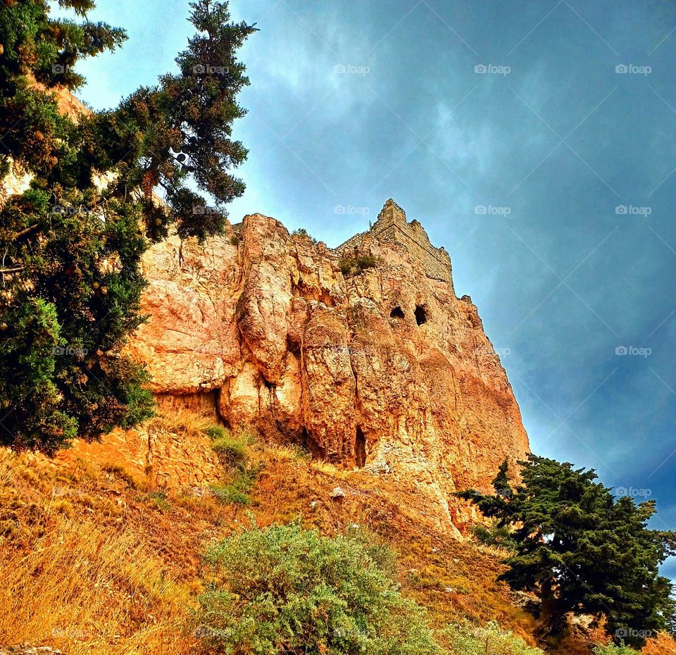 This photo showcases the Rocher de Vitrolles, a striking rock formation characterized by its rugged, reddish-brown cliffs. The rocky surface is textured and weathered, with small caves or openings visible near the top.