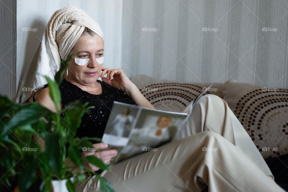Woman at home after shower relaxing on sofa reading magazine