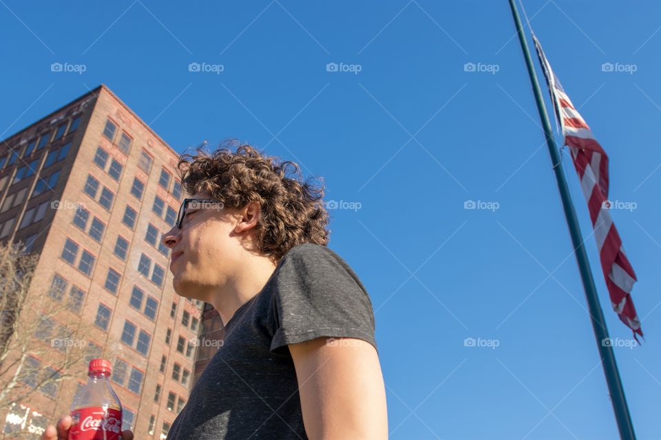 Man holding soda in front of building and American flag shot from low vantage point.