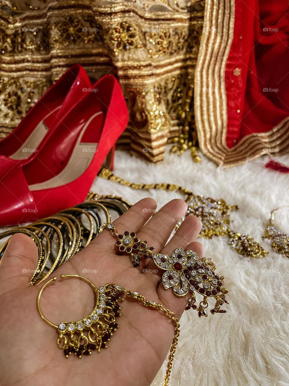 the bride's hand holds some of her wedding accessories with the dress and the shoes on the background.