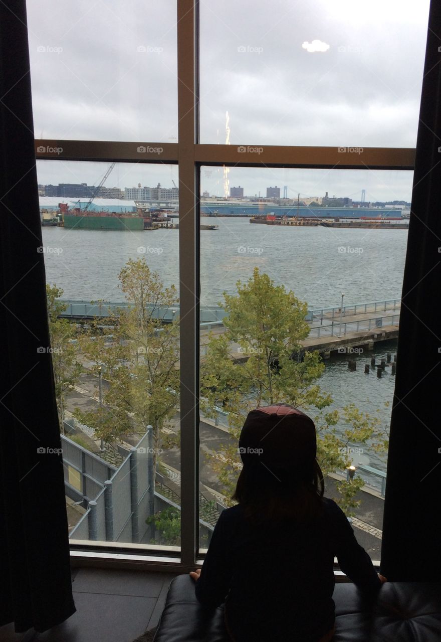 Just a little boy taking in the view from the window of the New York City harbor on a cloudy autumn day.
