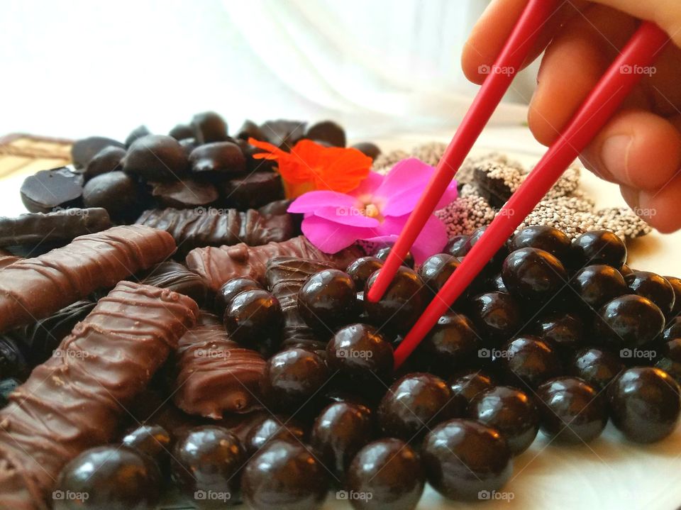 hand with red chopsticks selects from chocolate candies, plate with flowers