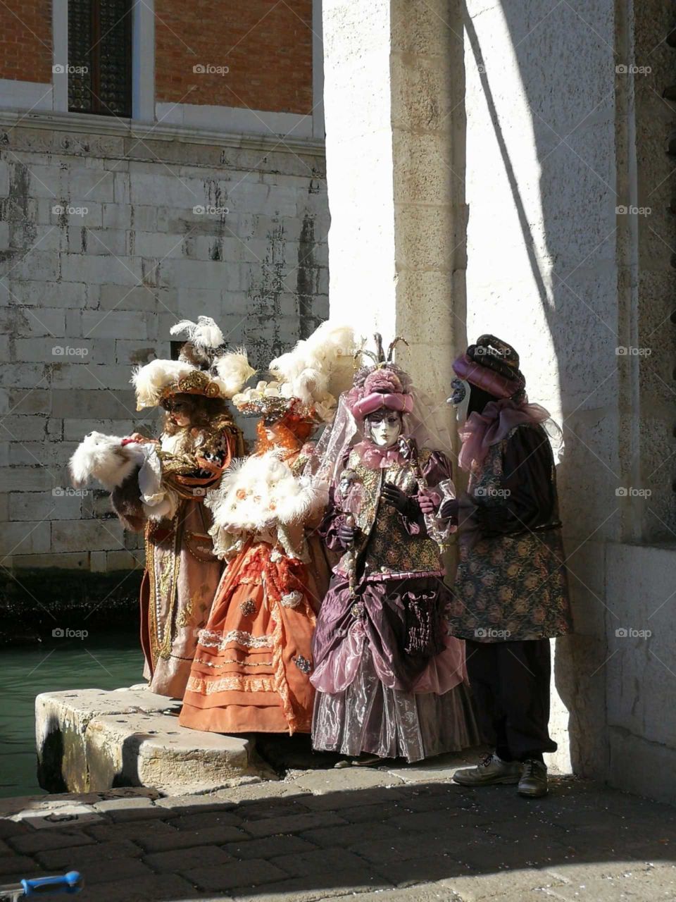 Venetian Carnival visitors in colorful costumes standing in front of a canal