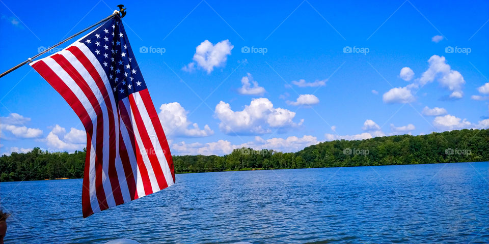 American Flag flying over water with clear blue skies.