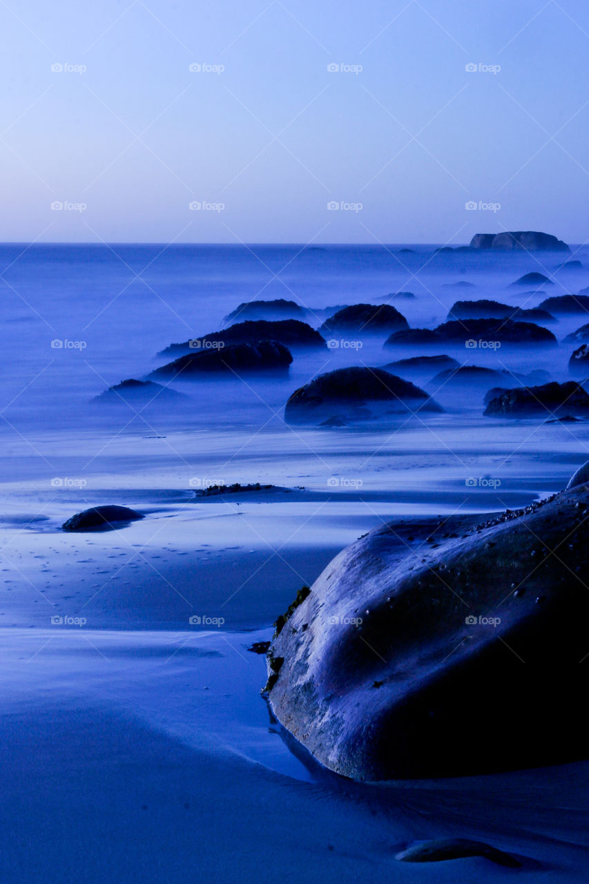 Mystical night seascape of boulders on a beach with waves.