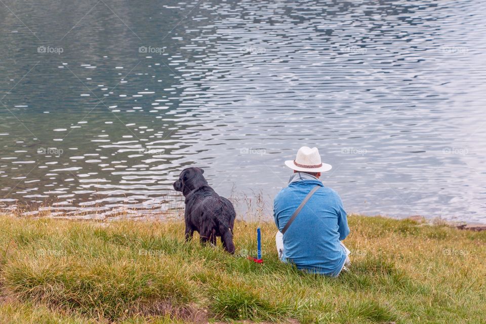Back side view of dog and its owner watching water and lake and enjoying the view. Picture taken in Rila Mountain - Seven Rila lakes, famous tourist attraction, Bulgaria
