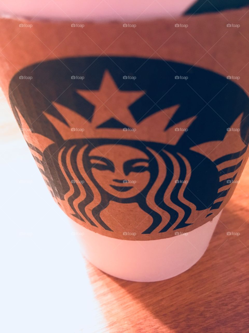 Starbucks coffee cup on wooden table in morning light. 