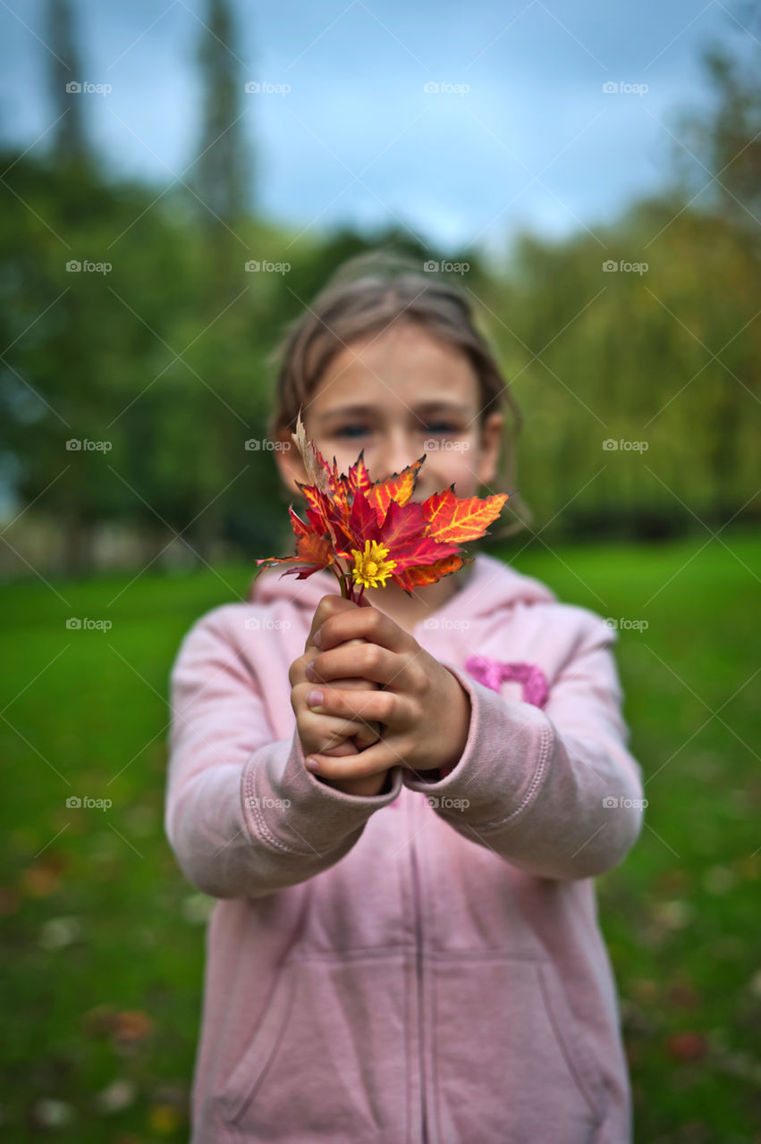 Fall. Autumn. Young girl holding little bouquet of autumn leaves in front of her.