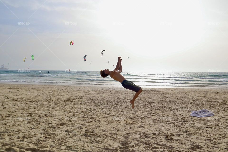 Kid doing somersault with kite surfer at background 