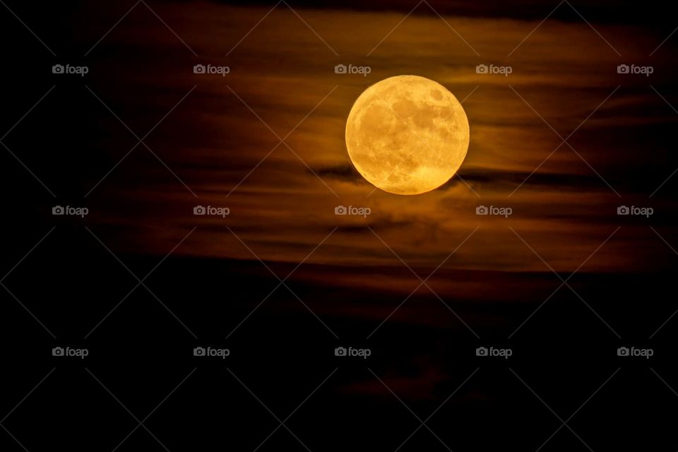 beautiful close up image of the autumn full moon glowing glowing a deep yellow orange with clouds around it leaving a sweeping yellow and orange pattern around the moon