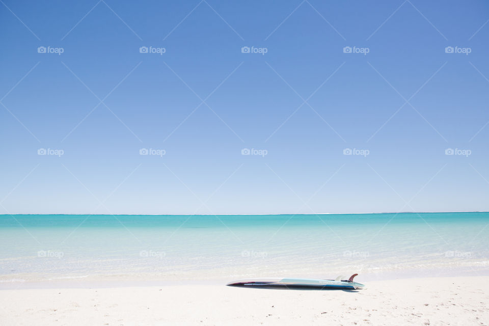 Stand up paddle board lying on white sand with turquoise blue water and blue skies 