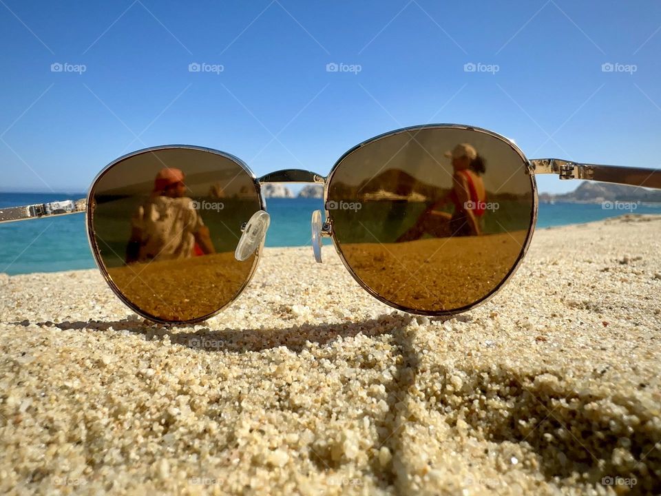 Sun glasses on the sand beach, while two persons are seeing each other through them.