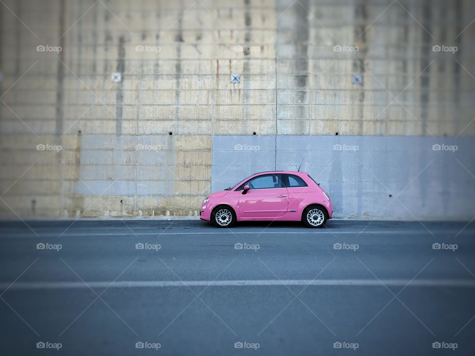 pink fiat 500 parked in front of a gray wall