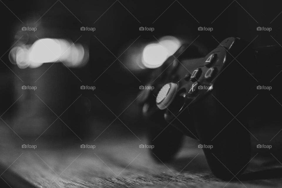Black and white low light Photo of playstation gamepad controller gaming accessories on a desk with blurry background bokeh.