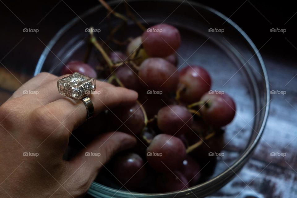 A hand with a sparkling ring takes grapes