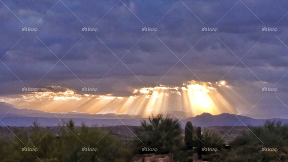 Stormy clouds give way to early morning sun rays shining down on the desert below.
