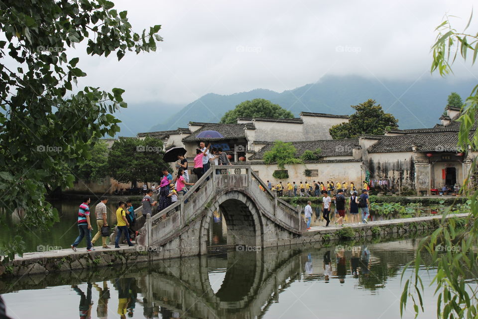 People walking across the bridge into a traditional village in China