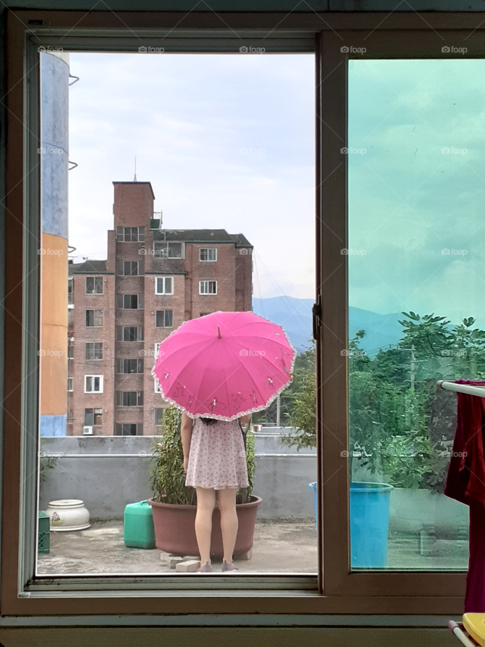 its  a summer time so a woman with umbrella is outside while checking the plants outside.