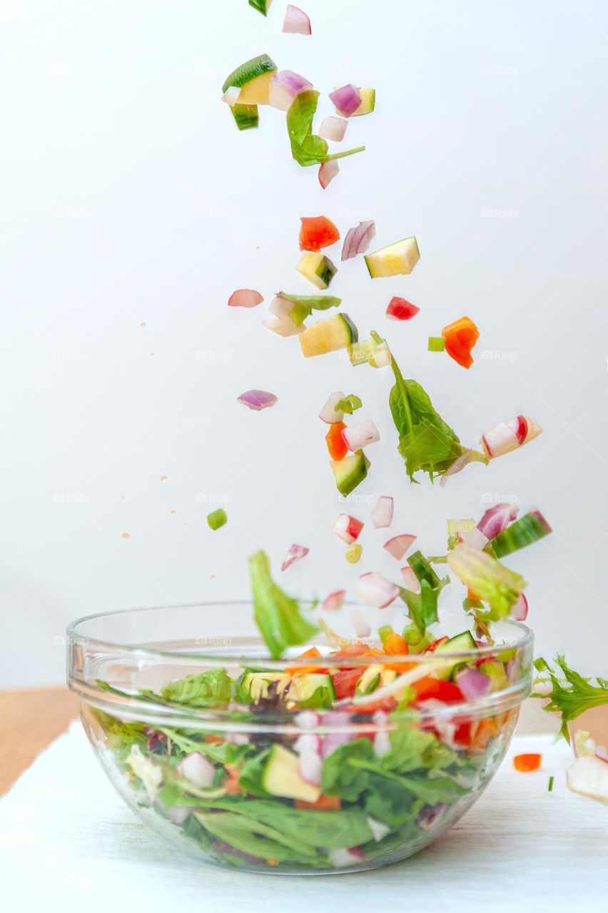 Pieces of fresh vegetables falling down into  glass bowl creating healthy salad.