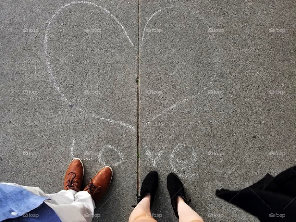 Couple stands by the word "Love" written on the sidewalk in chalk.