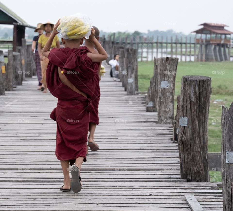 Myanmar local life style ,Little monk carry banana on his head to walk on U being bridge , the most longest wooden bridge in the world