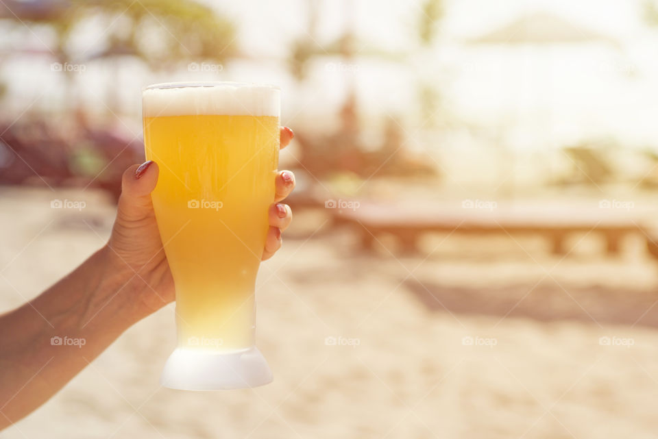 Hand of a woman holding a glass of beer on the beach