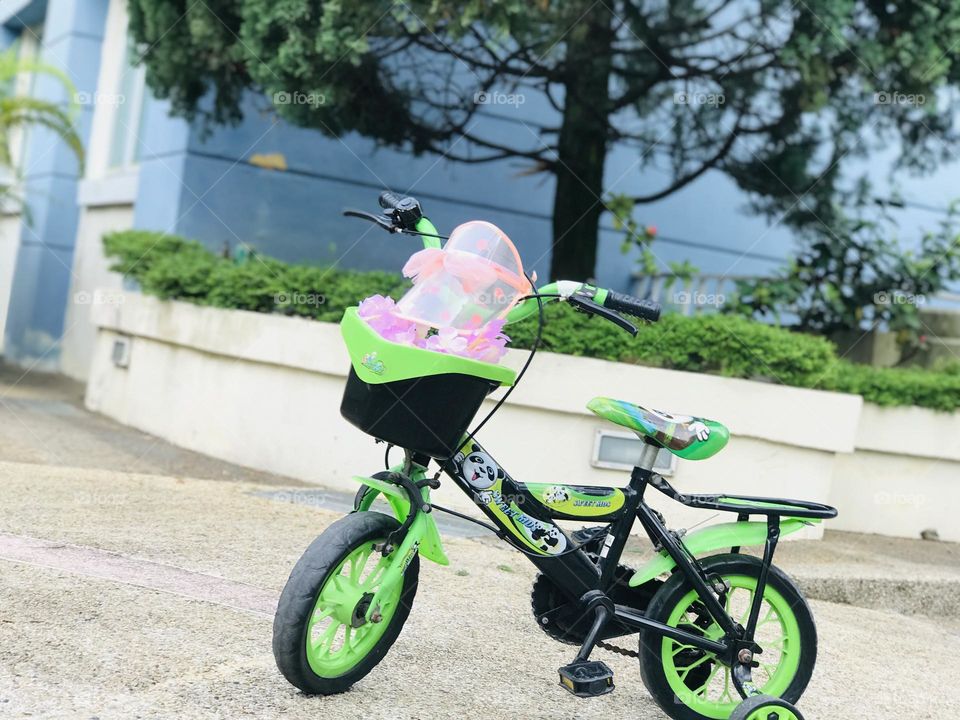 A green kids cycle with hat and pink flowers in basket 