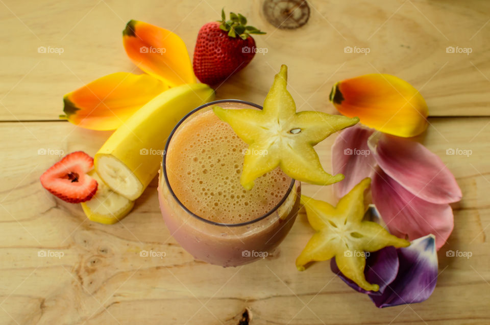 Beautiful healthy fruit smoothie background with fresh fruit banana, strawberry, starfruit, flower petals conceptual wellness self care healthy lifestyle photography