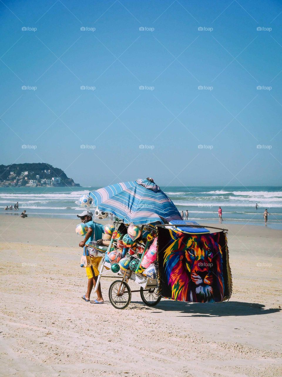 Beautiful Brazilian Beach, at Guarujá's Enseada Beach, sunny day . There's a Man with a cart, a shop cart, selling clothes, balls and umbrellas.