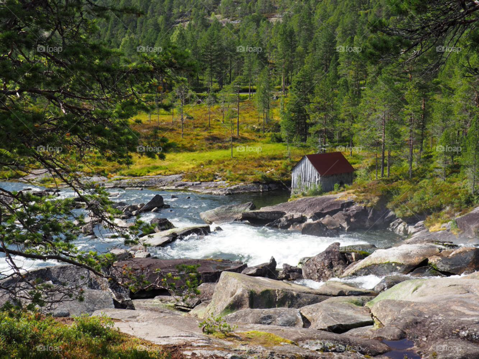 Gray cabin on river cascade in Norway