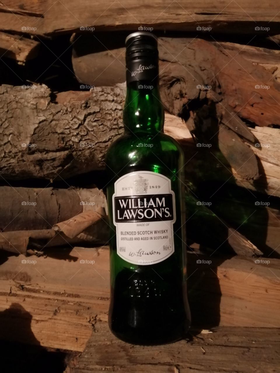 A green bottle of William Lawson's whiskey against the backdrop of wood-burning aspen pine lime