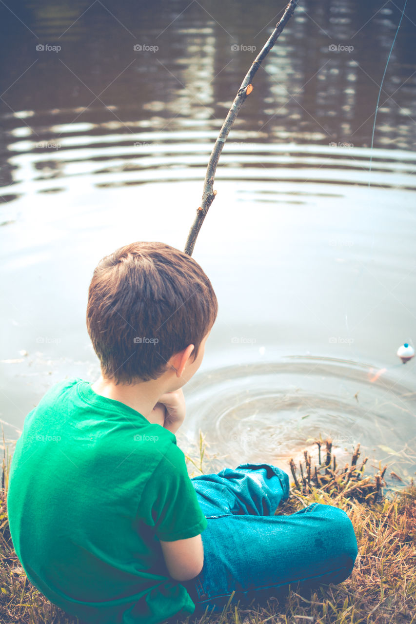 Young Boy Fishing at the Edge of a Pond with a Stick Pole