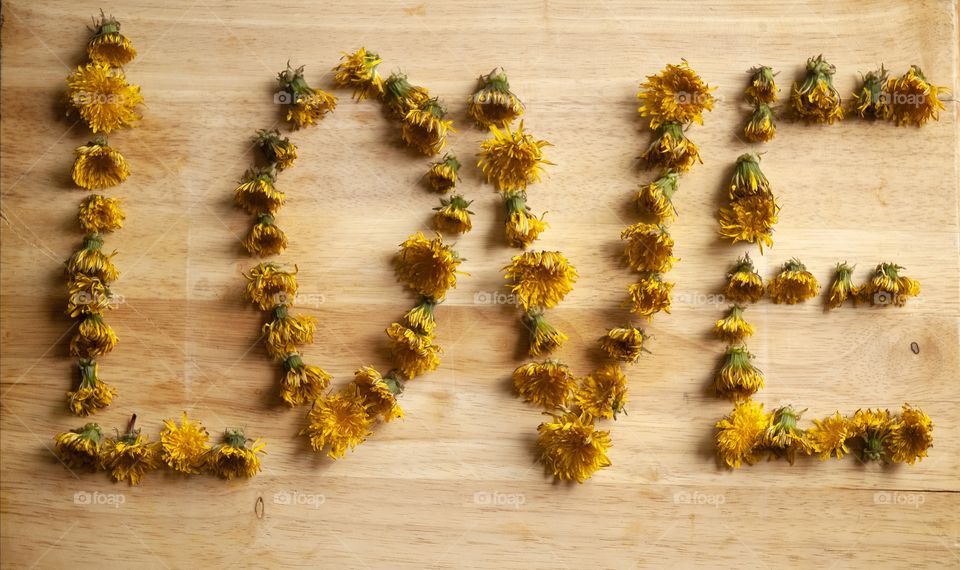 Dandelion flower heads are arranged on a wooden cutting board into the word love.