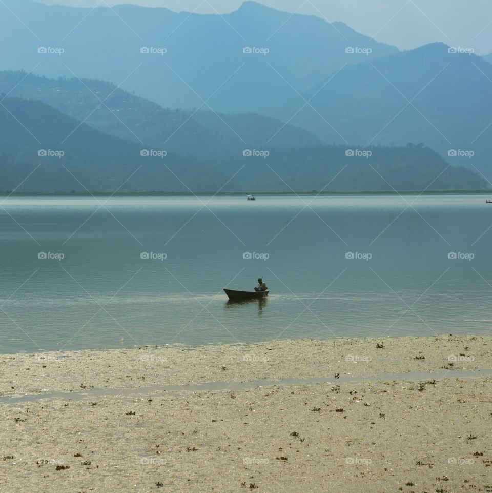 one man in a boat on a flat lake with hills in the background