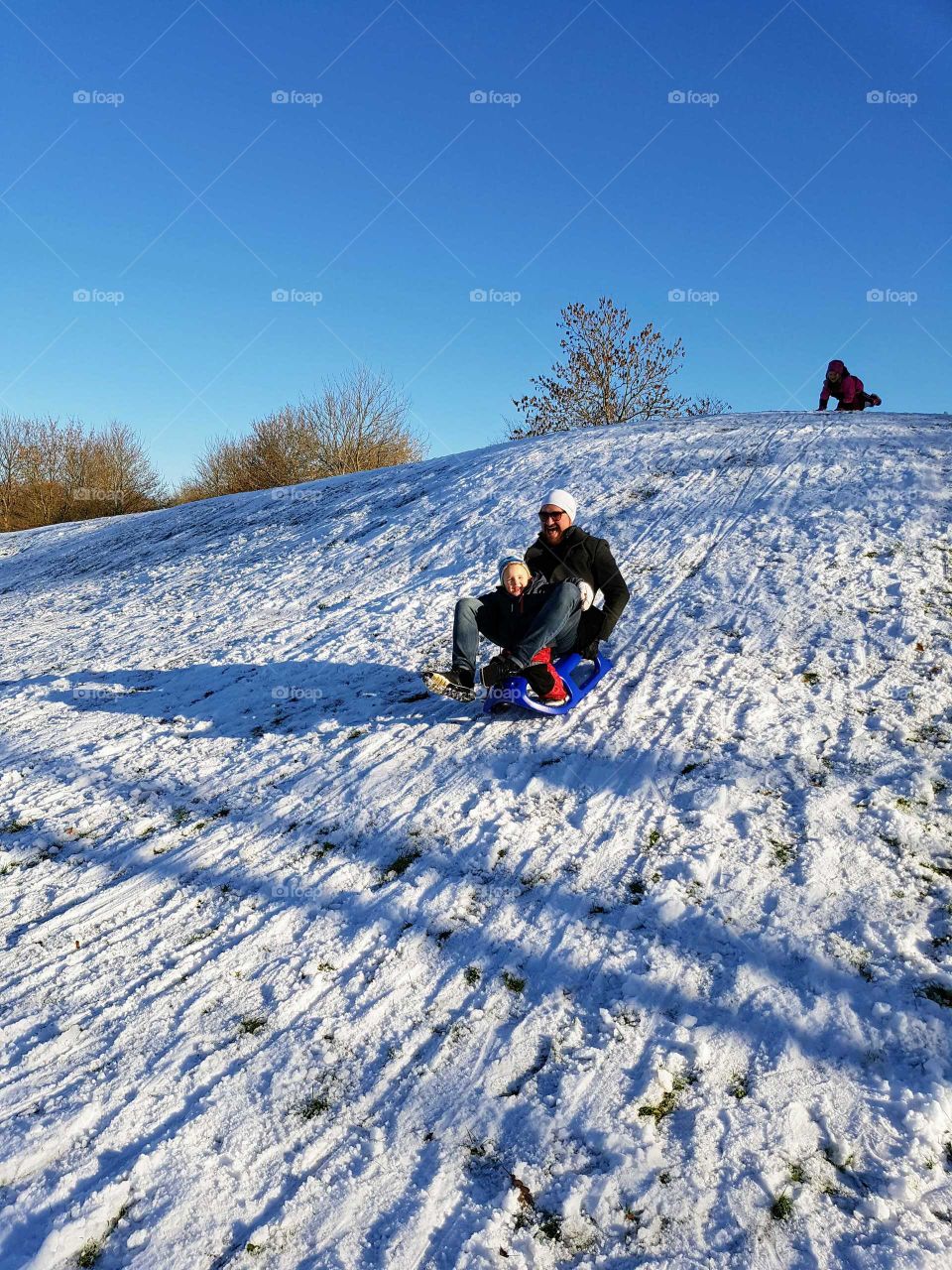 Father and son sledging down a snowy slope