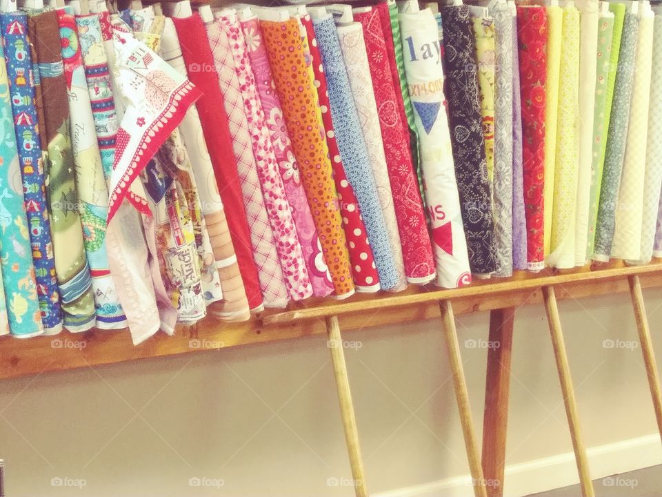 lower shelf of fabric rolls with a ladder leaning below. Nice colors and patterns.