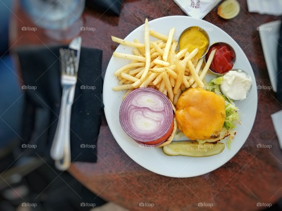 The Beauty and Colors of A Burger on a Plate with cheese, fries, tomato, onion, and a pickle
