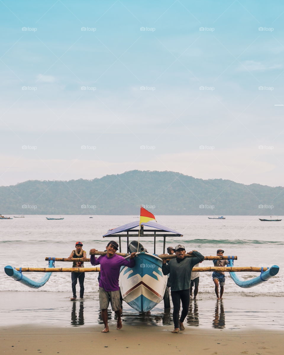 A group of people is working as a team to bring the boat back to the beach after fishing.