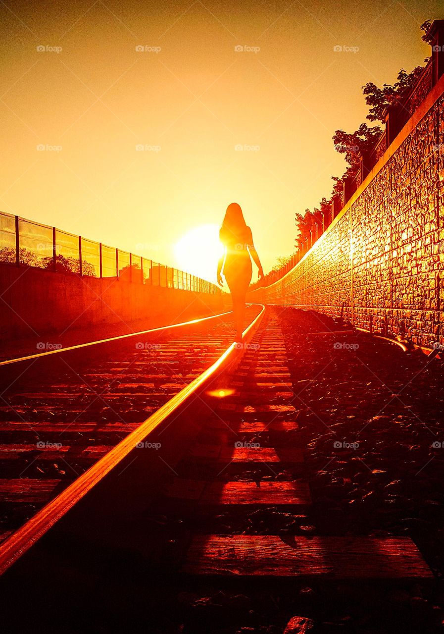 Woman is walking on railways in sunset