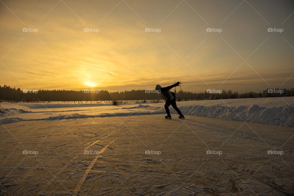 A man skating on the frozen lake ice at sunset