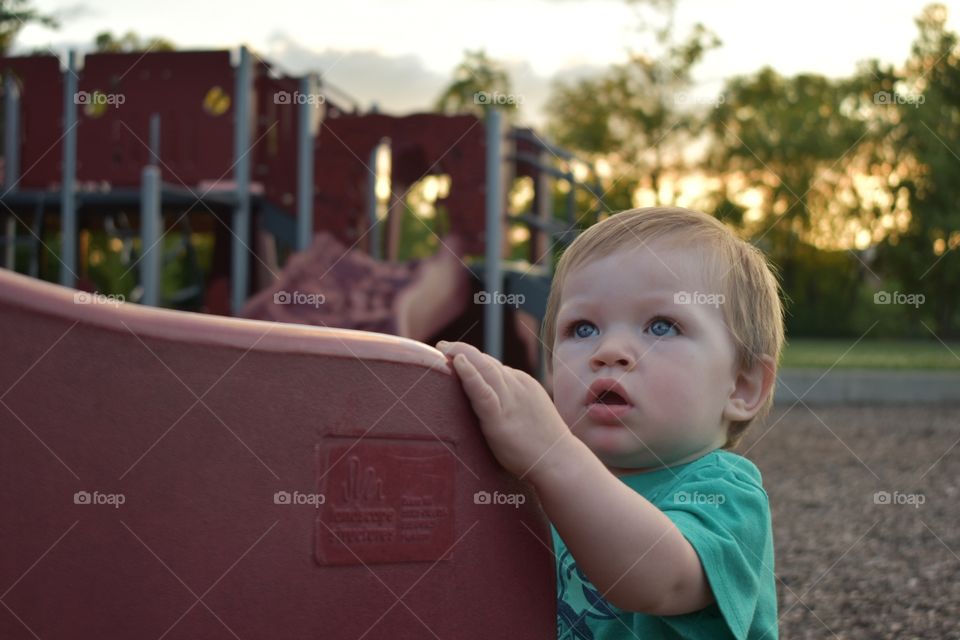 Cute toddler boy staring at older children playing 