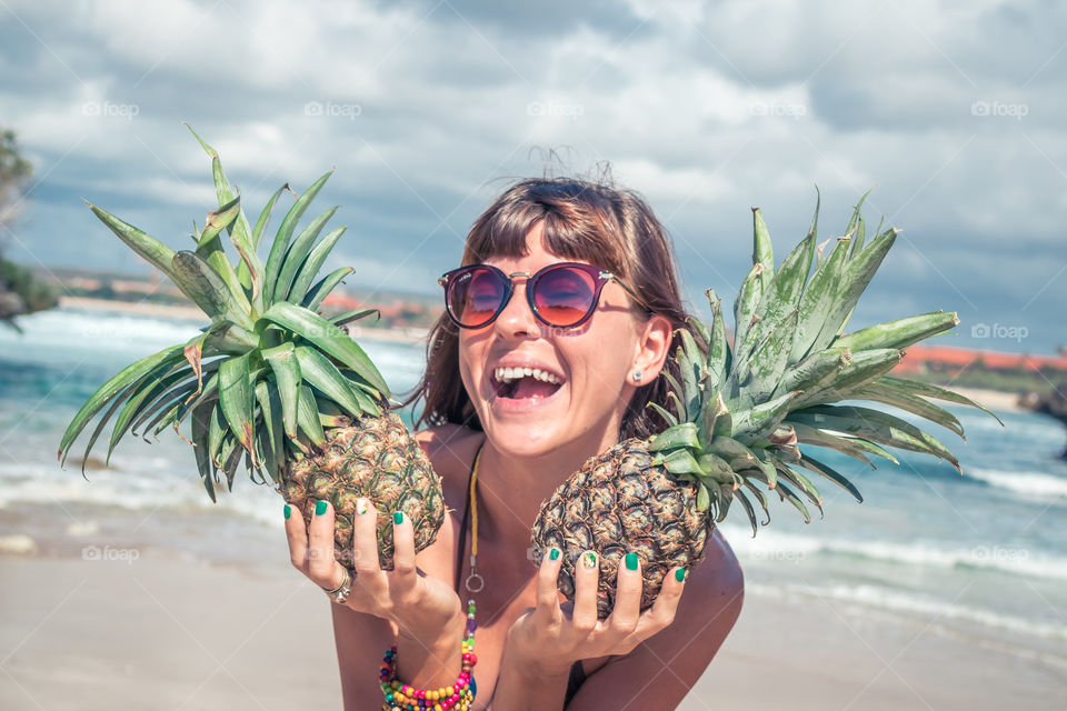 The girl laughs and holds pineapples in her hands. Bali island, Nusa-Dua beach.